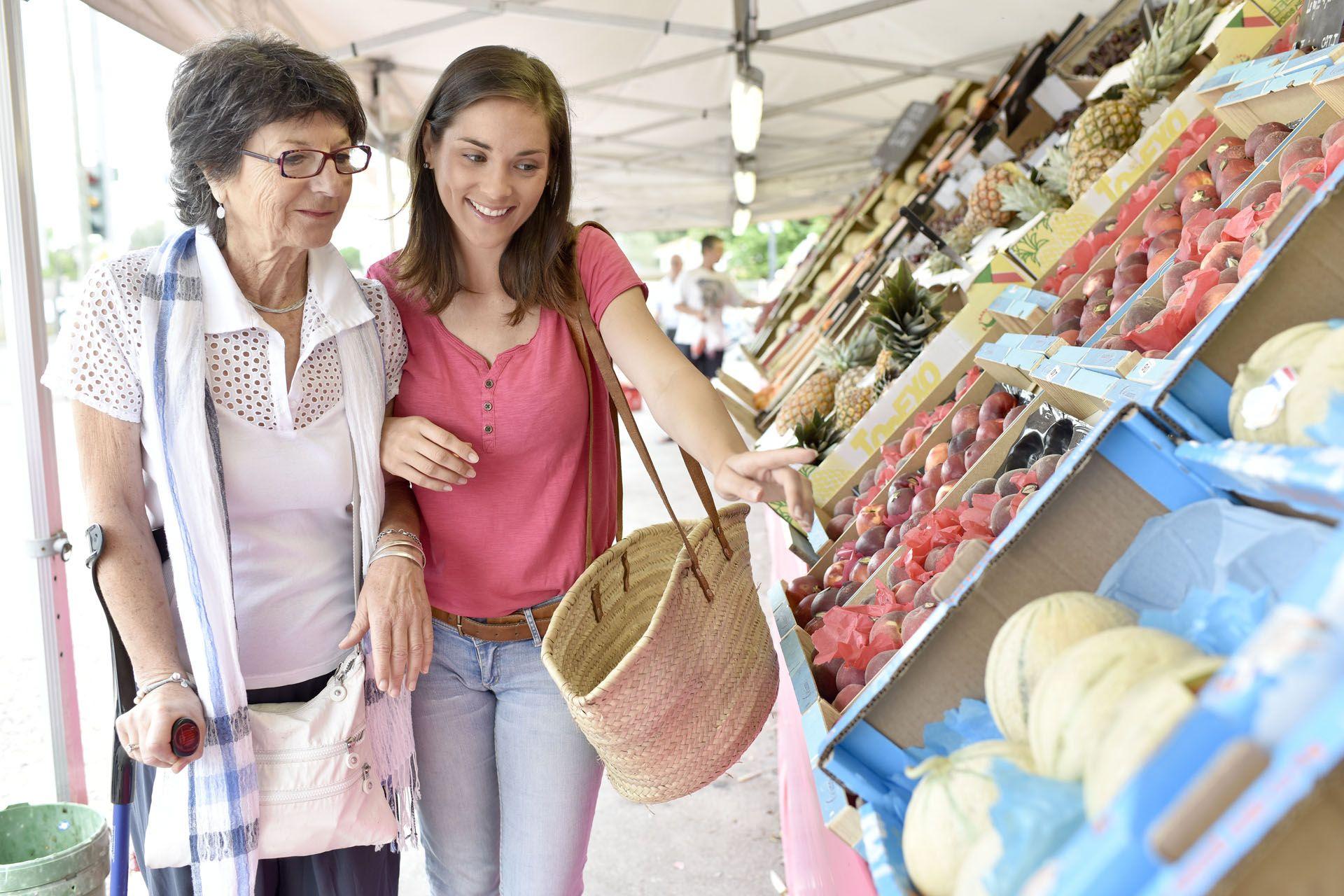 Une assistante de vie aux familles qui aide une personne agée à faire ses courses dans un marché