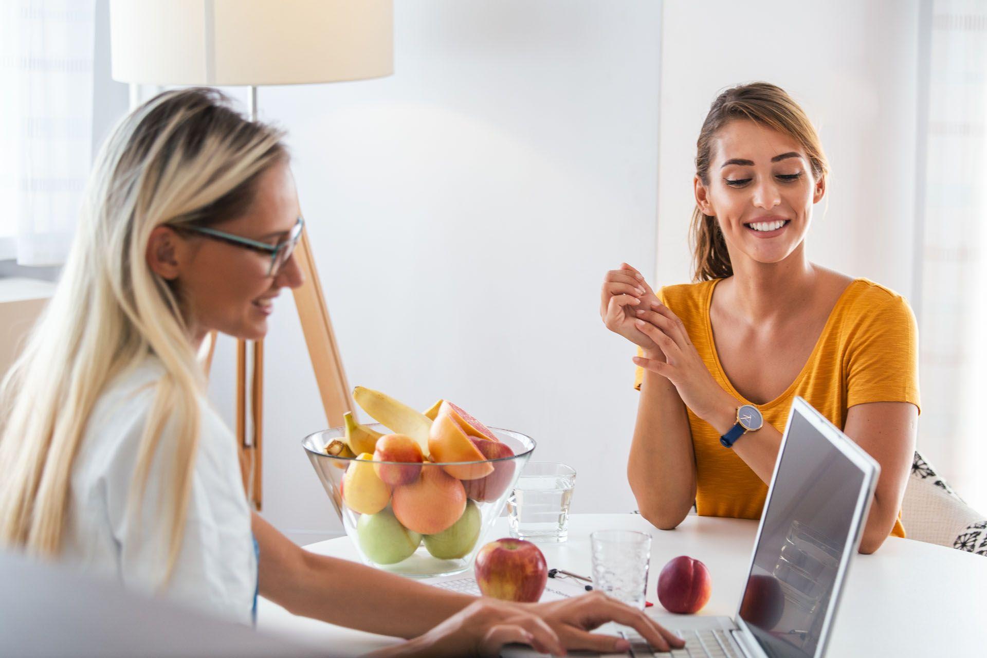 Une nutritionniste qui donne des conseils à sa patiente avec des fruits et légumes sur la table