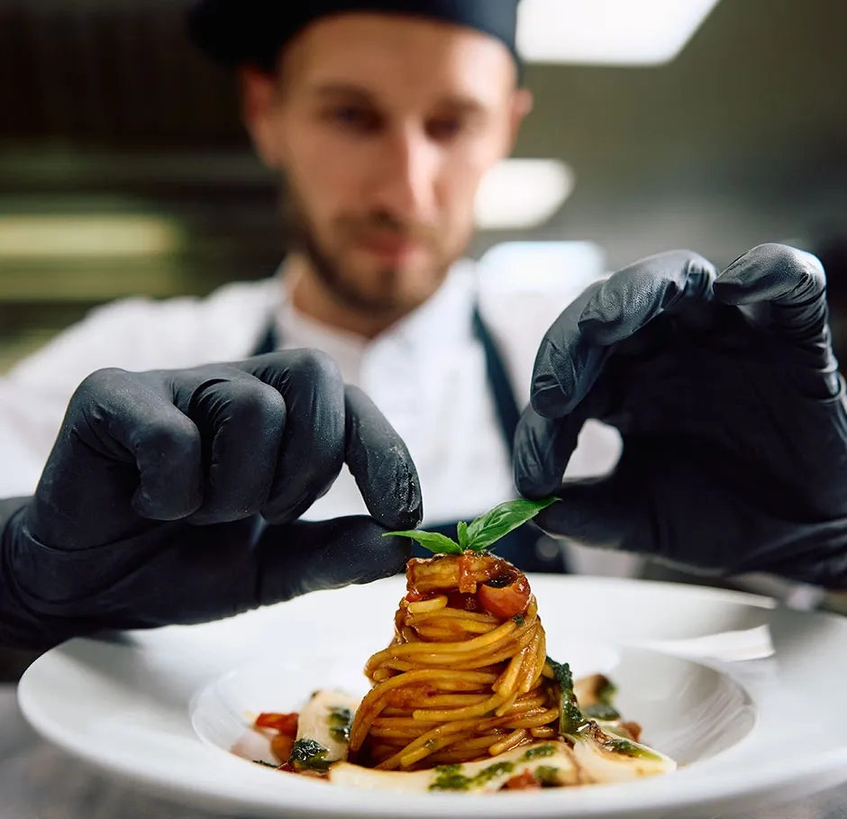 Apprenant en formation cuisine dressant un plat de pâtes gastronomique avec précision dans le cadre d’un projet de création d’entreprise en restauration