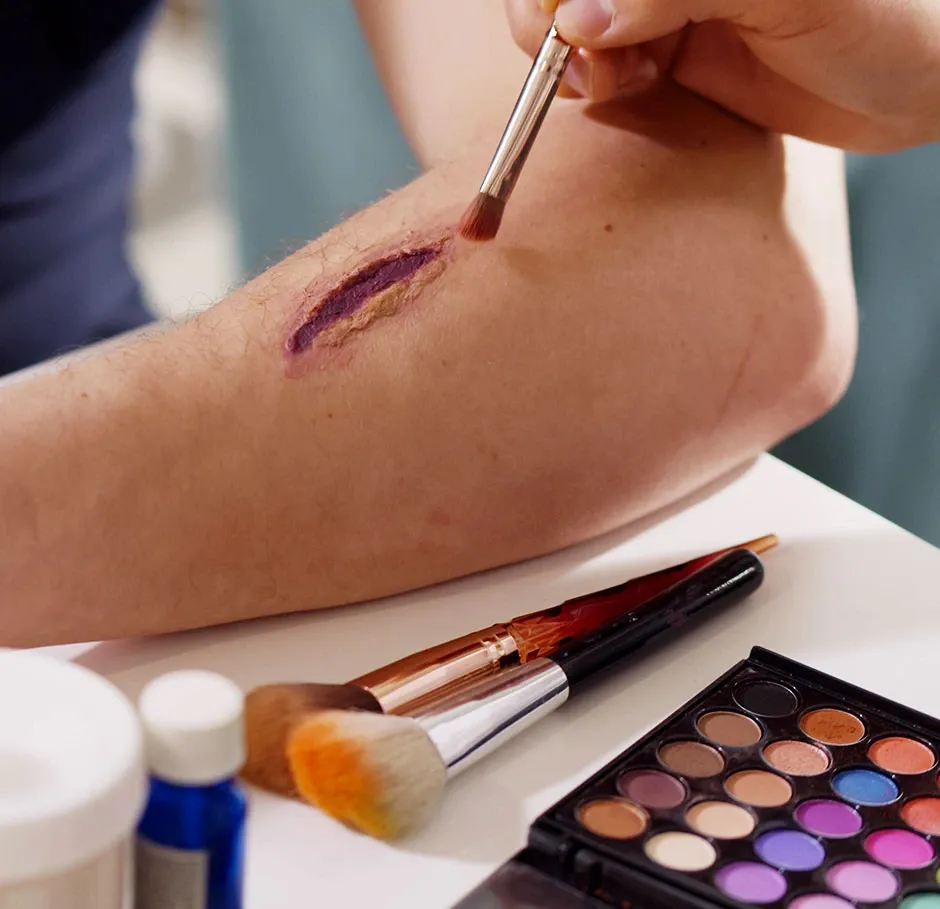 Apprenant en formation maquillage cinéma réalisant une fausse plaie avec des effets spéciaux sur l’avant-bras lors d’un atelier pratique