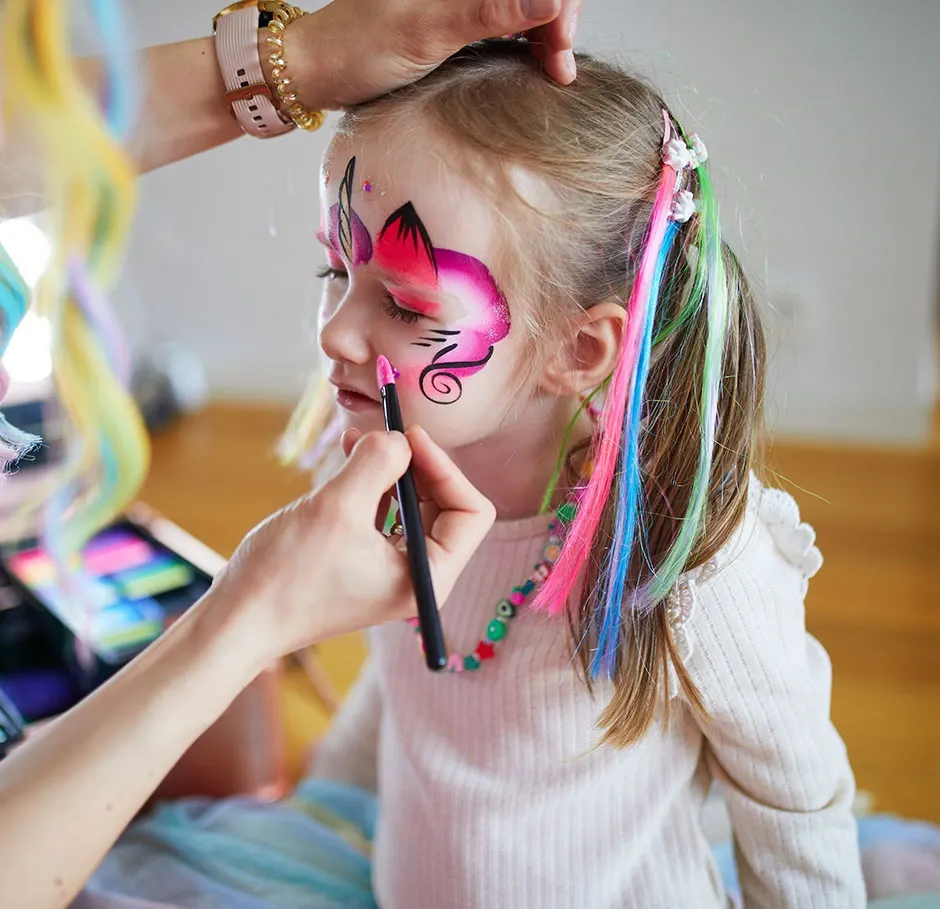 Apprenant en formation maquillage pour enfants réalisant un face painting coloré sur le visage d'une petite fille lors d'un atelier pratique